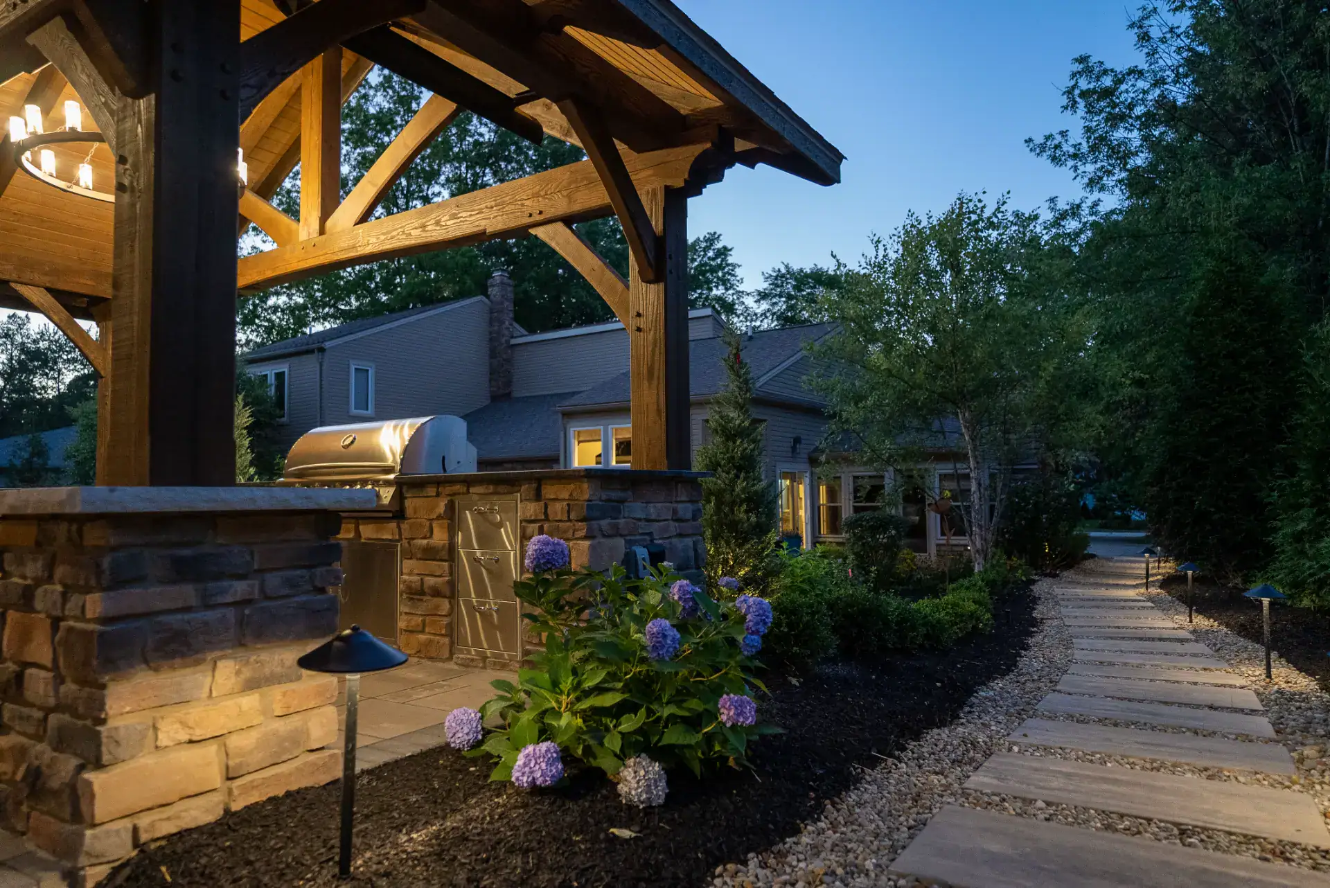 Outdoor kitchen under a timber pavilion with lit paver walkway in Pepper Pike, Ohio by TAB Property Enhancement